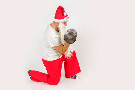 Christmas and New Years concept. Santa Claus is engaged in fitness, trains with a dumbbell. Isolated background.の写真素材