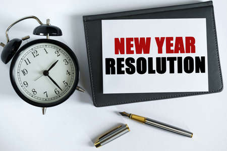 Business and positive concept. On the table there is a clock, a pen, a notebook and a card on which the text is written - NEW YEAR RESOLUTIONの写真素材