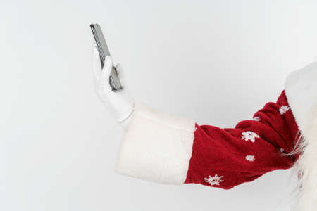 Christmas and New Years concept. Santa Claus holds a mobile phone in his hand. No face visible. Isolated backgroundの写真素材