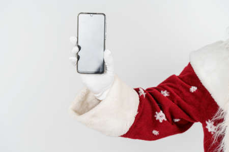 Christmas and New Years concept. Santa Claus holds a mobile phone in his hand. No face visible. Isolated backgroundの写真素材