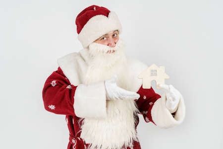 New Year and Christmas concept. Santa Claus keeps as a gift - a house. Isolated on light backgroundの写真素材