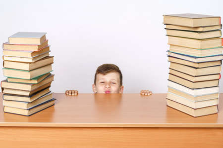 Education concept. The student is tired of lessons, hides and looks out from the table. He has books...