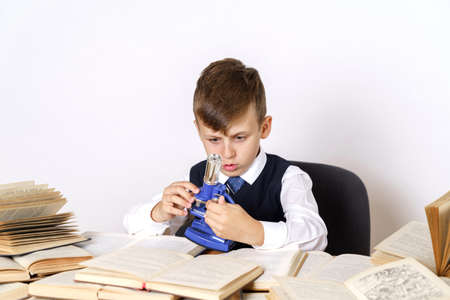 Education concept. The student does homework, studies the microscope. There are many open books on...