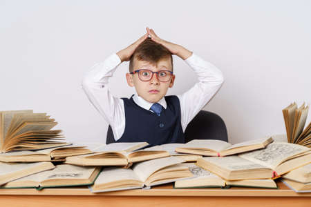 The student does his homework, holds his head with his hands and looks at the camera. There are many open books on the table.の写真素材