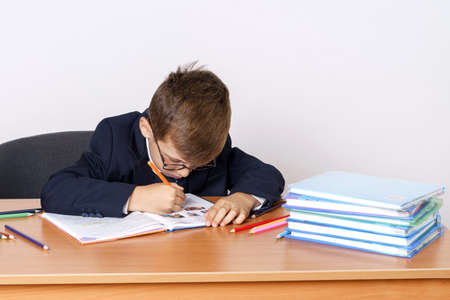 Education concept. The student sits at the table and writes. Books and pencils are on the table. Isolated on white background.の写真素材