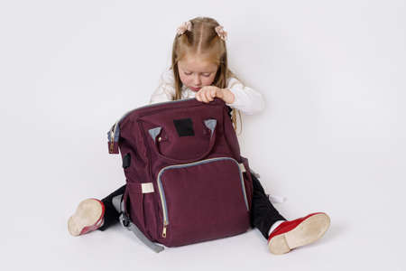 Children concept. The girl sits on the floor and looks inside the bag. Isolated over white...