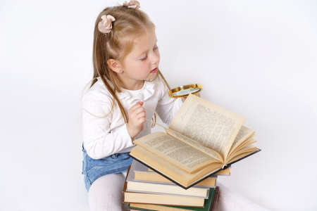 Education and people concept. Portrait of a teenage girl who sits near books with a magnifying glass. Isolated over white background.の写真素材