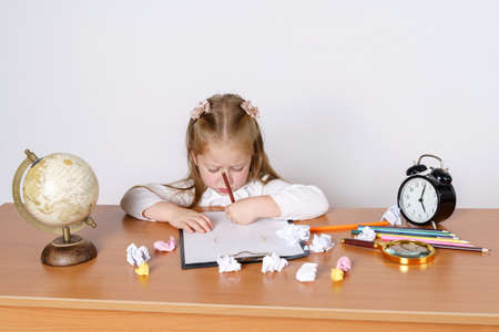 Education and kids concept. The girl sits at the table and draws on a sheet of paper with pencils....