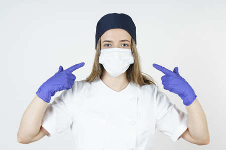Medicine and health concept. Young woman doctor points with her hands to a medical mask. Isolated over white background.の写真素材