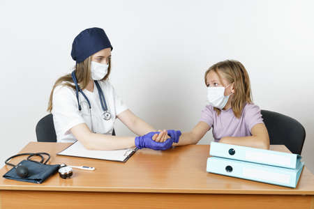 Medicine and health concept. Teenage girl at a pediatrician appointment. The doctor measures the pulse. Isolated over white background.の写真素材
