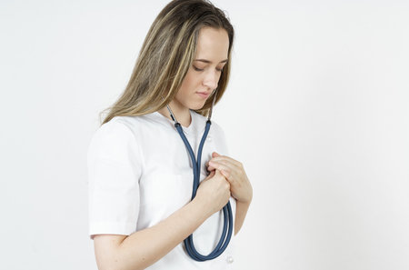 Medicine and health concept. Doctor woman listens with a stethoscope to her heart. Isolated on white background.の写真素材