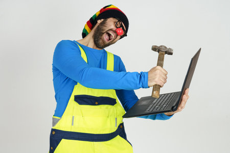 Humor and communication concept. A clown in a bright suit holds a laptop in his hands, hits it with a hammerの写真素材