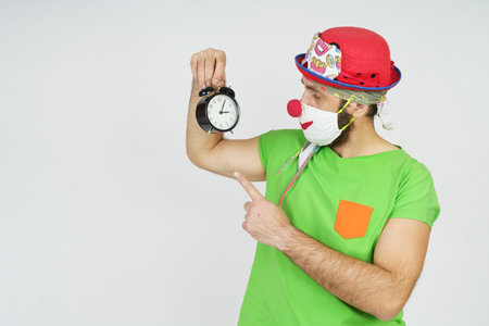Holiday and fun concept. The clown holds an alarm clock in his hands. Isolated on white