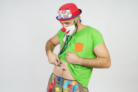 Holiday and fun concept. The clown is playing doctor, listening to his stomach with a stethoscope....