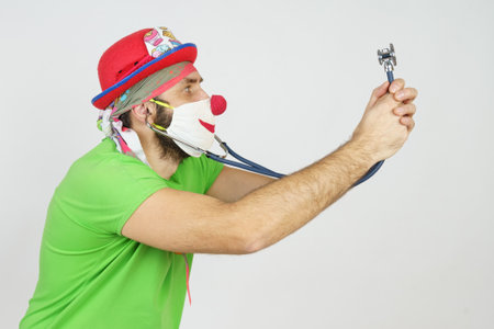 Holiday and fun concept. The clown plays doctor, bugs himself with a stethoscope. Isolated on whiteの写真素材