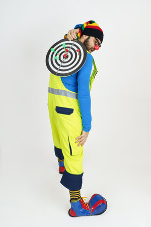 Celebration and communication concept. The clown holds a target with darts behind his back. Isolated...