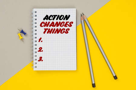 Business and finance. On a yellow-gray background are pencils, buttons and a notebook in which it is written - ACTION CHANGES THINGSの写真素材