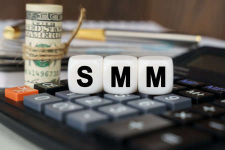 Business and finance concept. There are cubes on the calculator that say - SMM. Nearby out of focus - dollars, notebook and penの写真素材