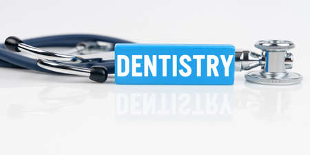 Medicine and health concept. On a white reflective surface is a stethoscope and a blue block with the inscription - DENTISTRYの写真素材