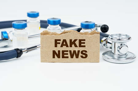 Medicine and health concept. On a white table lie ampoules, a stethoscope and a cardboard with the inscription - FAKE NEWSの写真素材