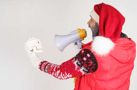 New Year and Christmas concept. Santa Claus speaks into a loudspeaker, in the second hand is a skull.の写真素材