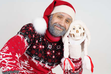 Holiday and Christmas concept. Santa Claus holds a skull in his hand and looks at the cameraの写真素材