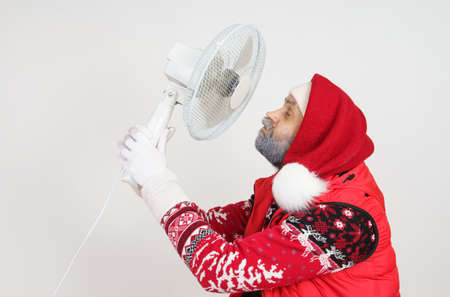 Holiday and Christmas concept. Santa Claus is cooled with a fan