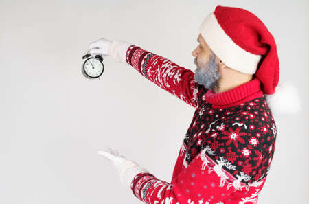 Holiday and Christmas concept. Santa Claus points to the clock before Christmas. Santa hat on the clockの写真素材