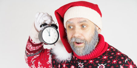 Holiday and Christmas concept. Santa Claus holds an alarm clock near his ear.