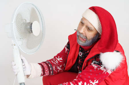 Holiday and Christmas concept. Santa Claus is cooled with a fan