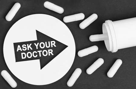 Medicine concept. Pills on a black background. They are indicated by a circle with an arrow, inside which it is written - ASK YOUR DOCTORの写真素材