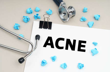 Medicine concept. On the table is a stethoscope, a pen, blue crumpled pieces of paper and a sign with the inscription - ACNEの写真素材