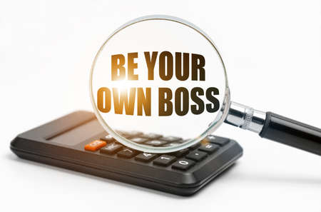Business and finance concept. On the table is a calculator and a magnifying glass, inside which the inscription - Be Your Own Bossの写真素材