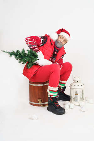 Christmas and New Year concept. Santa Claus sits on a barrel and holds a Christmas tree in his...
