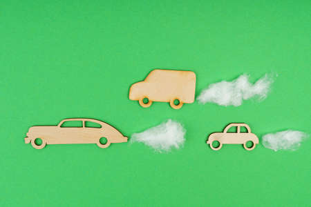 Environmental concept. Wooden cars with traces of CO2 emission - cotton wool. Isolated on a green background.の写真素材