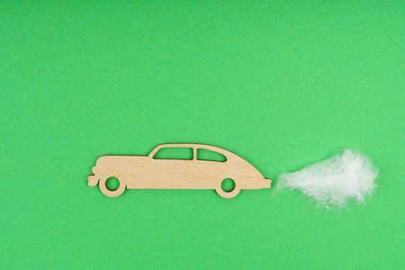 Environmental concept. Wooden car with traces of CO-2 emissions - cotton wool. Isolated on a green background.の写真素材