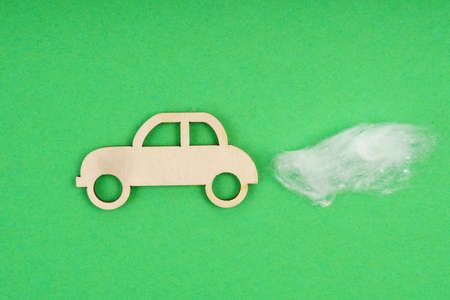Environmental concept. Wooden car with traces of CO-2 emissions - cotton wool. Isolated on a green background.の写真素材