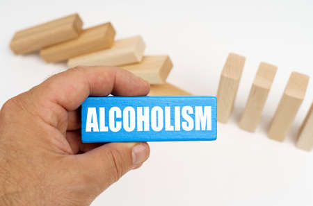 Medicine and health concept. In the background there are wooden planks - half are standing, half are lying. In the hands of a blue plaque with the inscription - ALCOHOLISMの写真素材