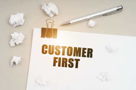 Economy and business concept. On a gray surface, a pen, crumpled paper and a sheet with the inscription - Customer Firstの写真素材