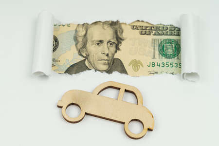 Business and transportation concept. On a white sheet of paper a wooden car, dollars in the window.の写真素材