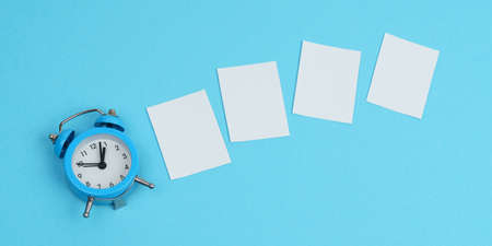 On a blue background, an alarm clock and white pieces of paper. Mockupの写真素材