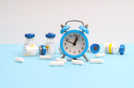 Medicine concept. On a white and blue background, an alarm clock, pills and jars with injectionsの写真素材