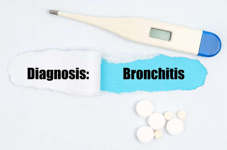 Medical diagnosis. A gap is made in the middle of the white sheet, inside of which there is an inscription - Bronchitis on a blue background. On the sheet is a thermometer and pills.の写真素材