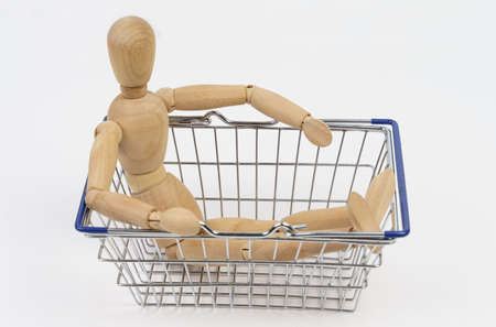 Business concept. The wooden man sits in a shopping basket. Isolated on white background.の写真素材