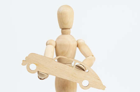 Business and travel concept. The wooden man holds a car in his hands. Isolated on white background.の写真素材