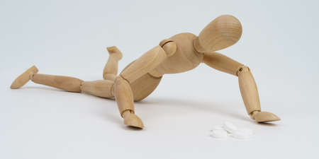 Medicine and addiction concept. The wooden man crawls for pills. Isolated on white background.