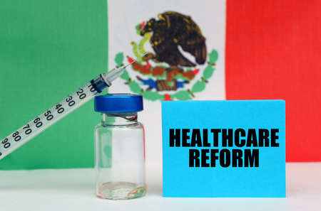 Medicine concept. Vaccine, syringe and blue plate with the inscription - HEALTHCARE REFORM. In the background the flag of Mexicoの写真素材