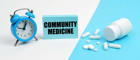 Medicine and health concept. On a blue surface are pills, on a white surface an alarm clock and a plate with the inscription - Community Medicineの写真素材