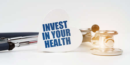 Medical concept. There is a stethoscope on the white surface, next to it there is a heart-shaped plate with the inscription - INVEST IN YOUR HEALTHの写真素材