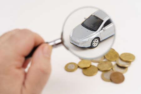 Car insurance. A man looks at a car through a magnifying glass, there are coins nearby. Isolated on...